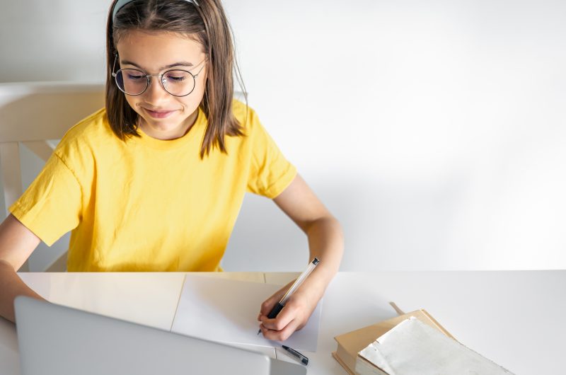 a teenage girl does her homework while sitting with books and a laptop.