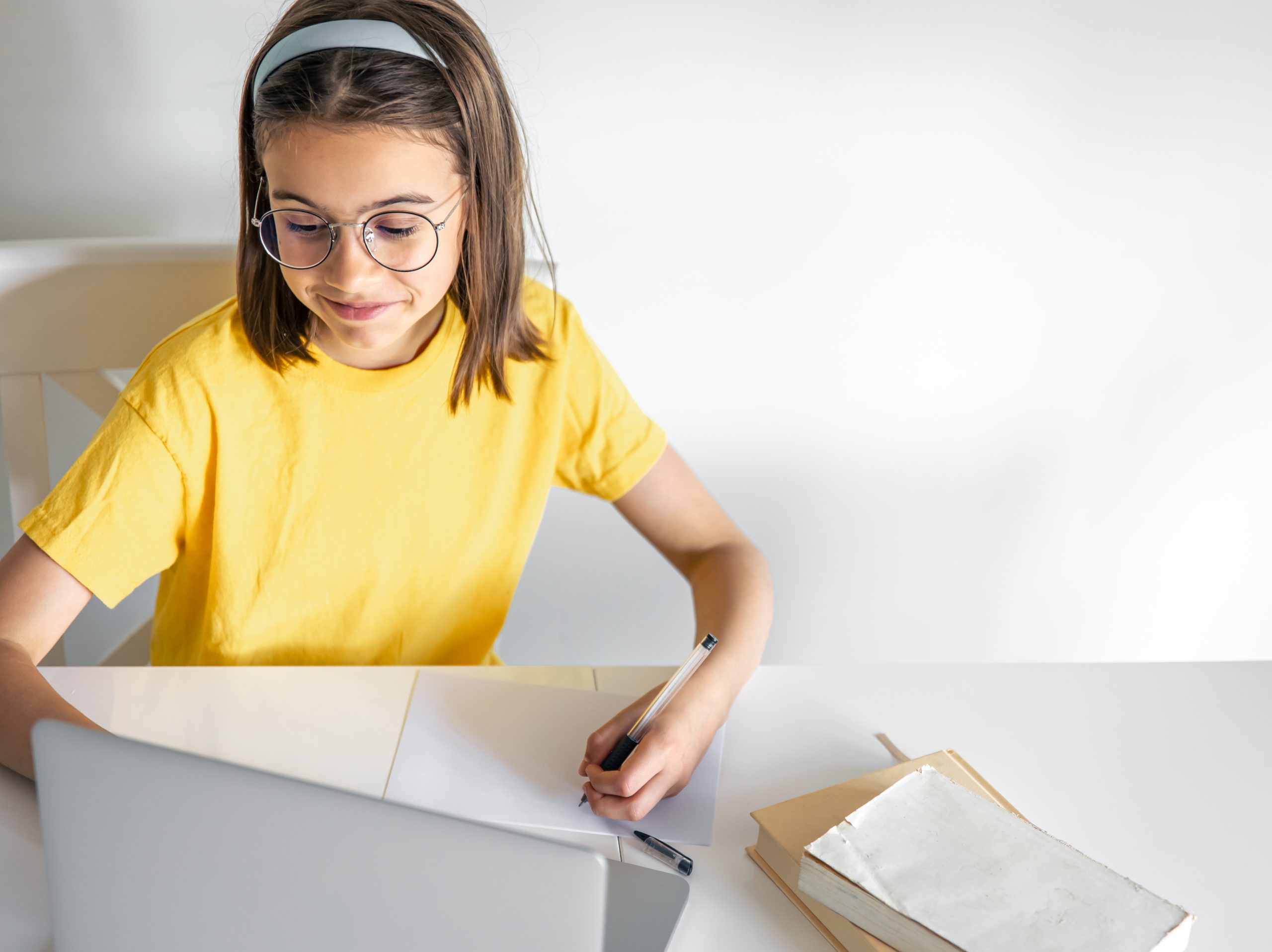a teenage girl does her homework while sitting with books and a laptop.